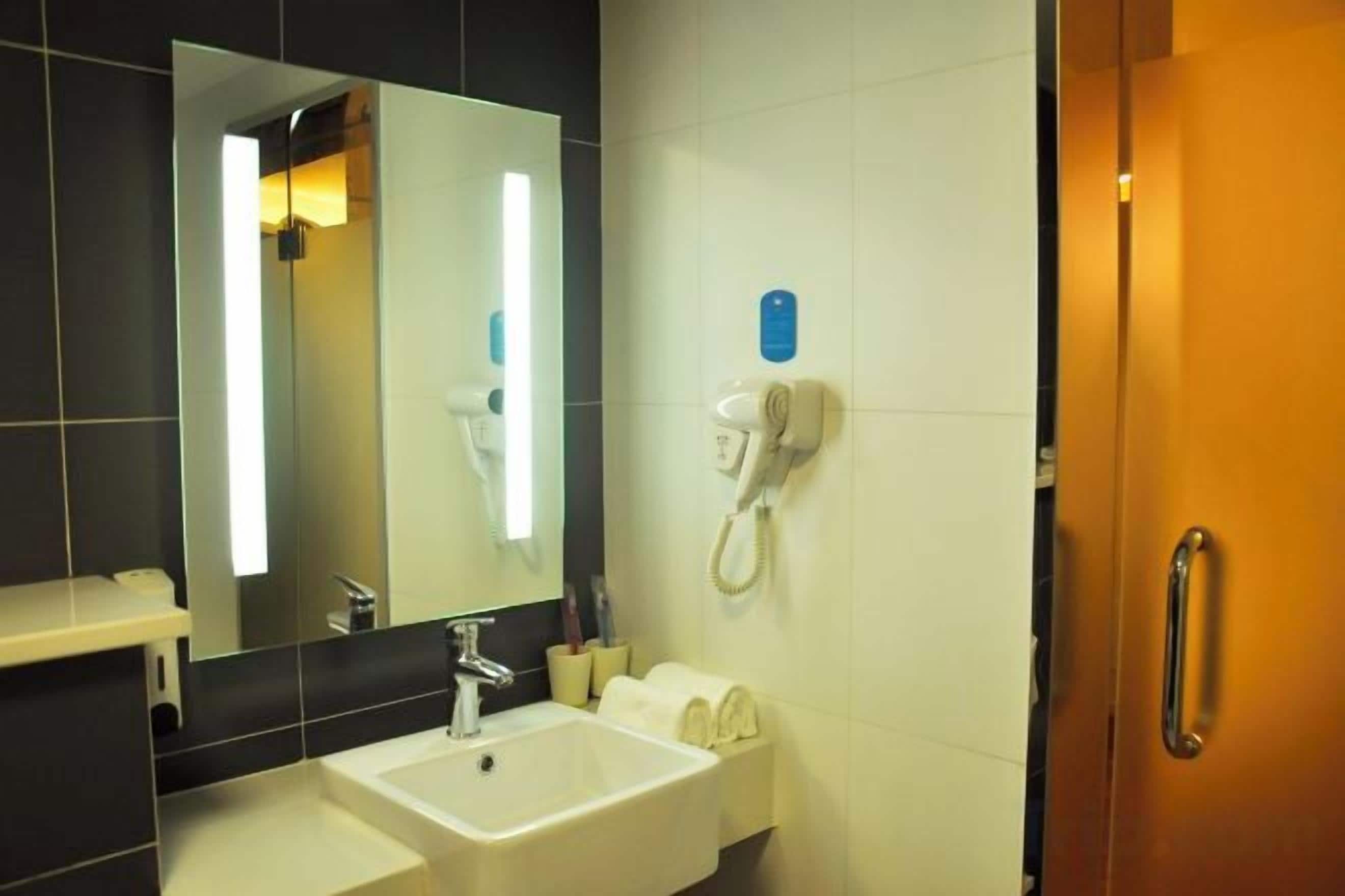 A hotel bathroom with a sink, mirror, and a hairdryer mounted on the wall.