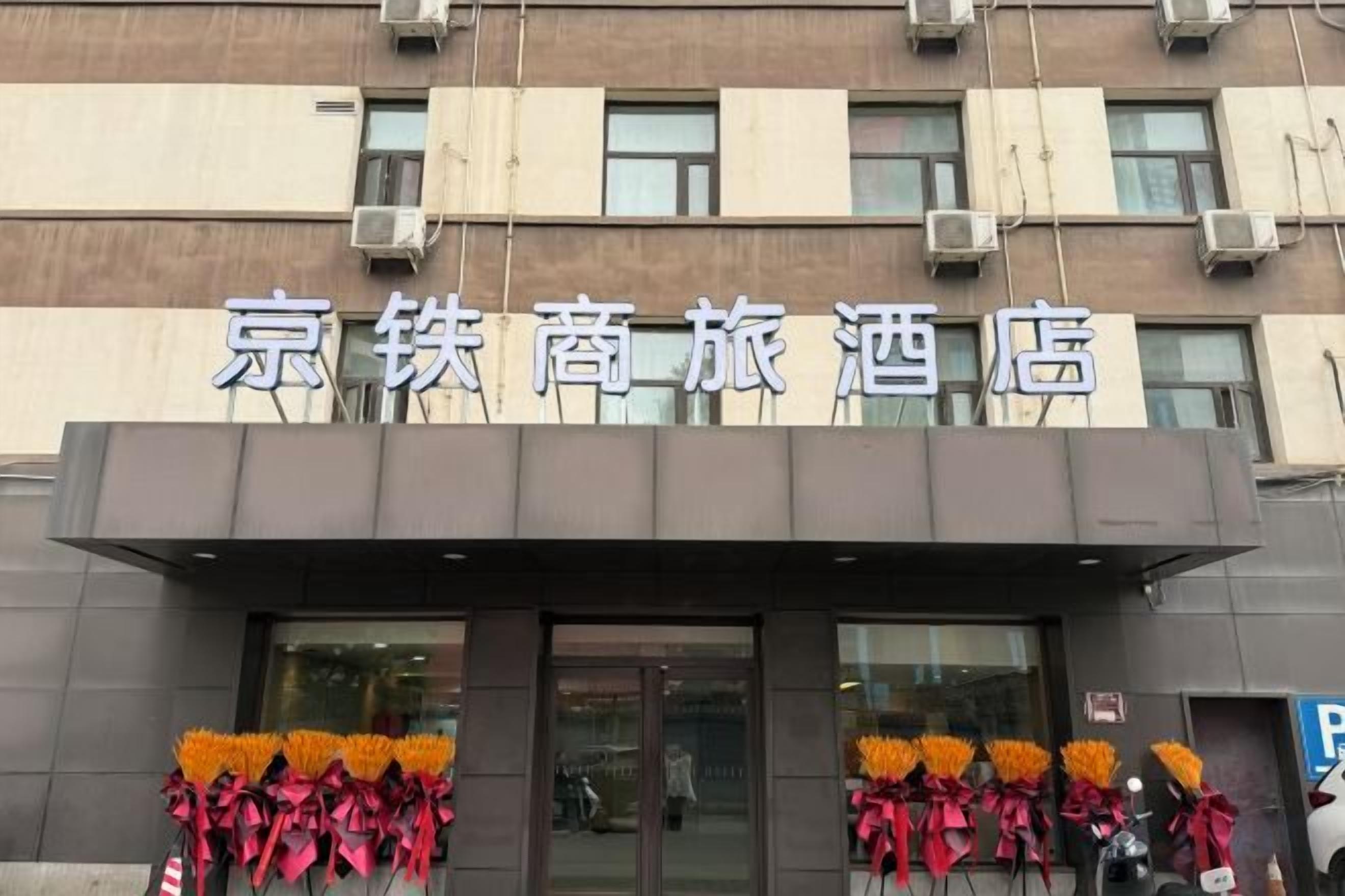 A hotel entrance with a sign above the door and decorative flowers on either side.