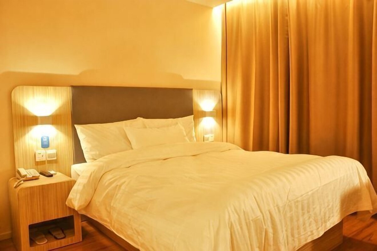 Una habitación de hotel con una cama, lámparas de noche, una mesita de noche y una cortina.