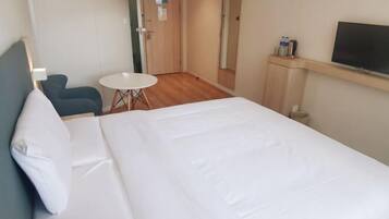 Habitación de hotel con una cama grande, una mesita redonda pequeña, una silla, un televisor y un espejo.