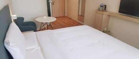 A hotel room with a large bed, a small round table, a chair, a TV, and a mirror.