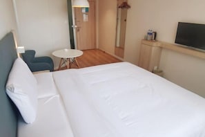 A hotel room with a large bed, a small round table, a chair, a TV, and a mirror.