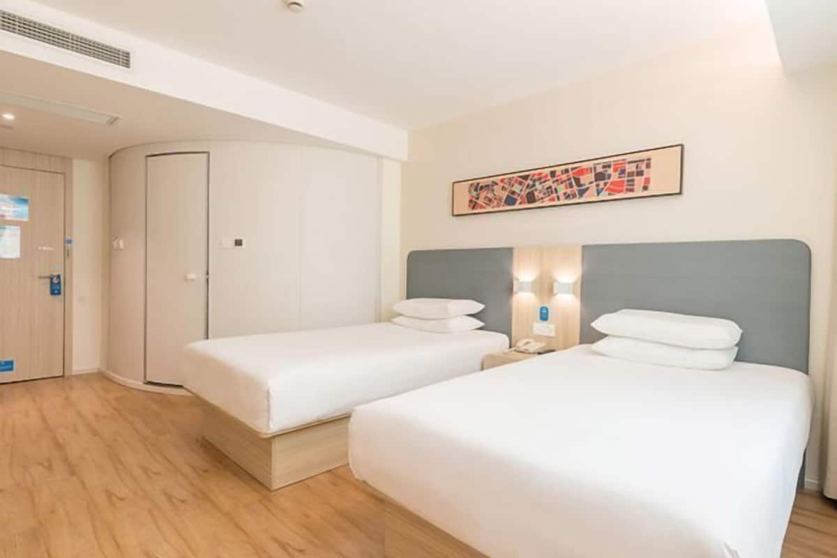 Une chambre d’hôtel avec deux lits simples, une armoire, un tableau au mur et une table de chevet avec une lampe.