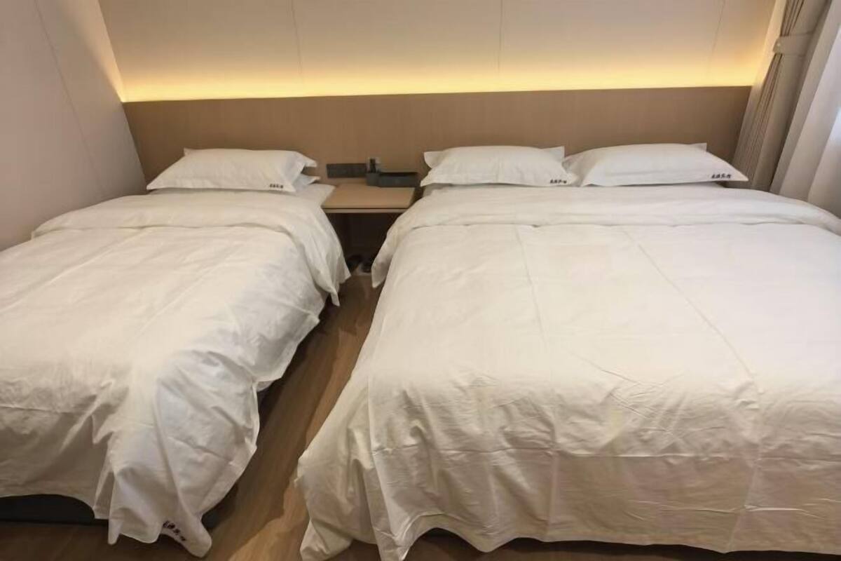 Hotellihuone, jossa on kaksi erillistä sänkyä, yöpöytä ja sängynpääty, jossa on sisäänrakennettu valaistus.