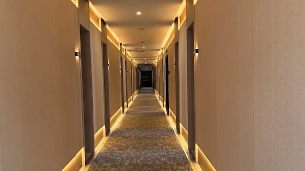Ein langer, schmaler Hotelgang mit Teppichboden und warmer Beleuchtung.