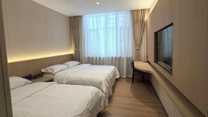 Ein Hotelzimmer mit zwei Betten, einem Schreibtisch, einem Sessel, einem Fernseher und einem Fenster mit Vorhängen.
