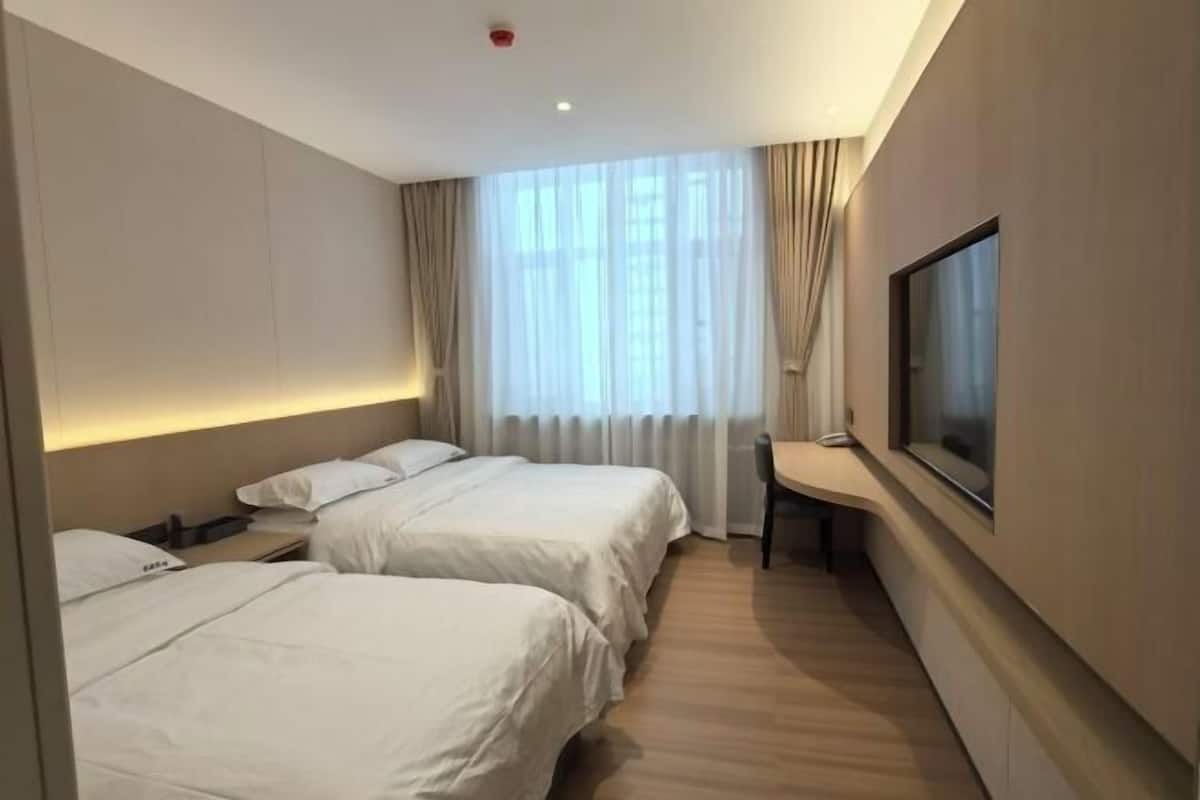 Hotellihuone, jossa on kaksi sänkyä, työpöytä, tuoli, televisio ja ikkuna, jossa on verhot.