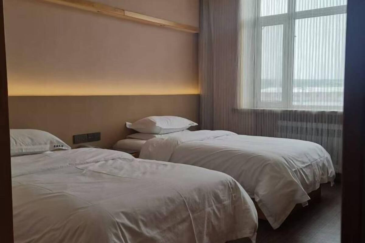 Hotellihuone, jossa on kaksi sänkyä, ikkuna, jossa on verhot, ja puinen pääty.
