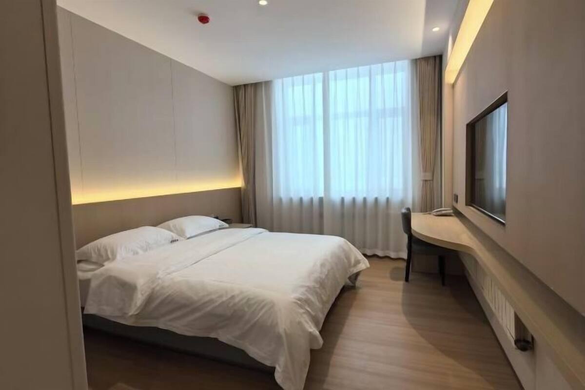 Hotellihuone, jossa on sänky, työpöytä, tuoli, televisio ja ikkuna, jossa on verhot.