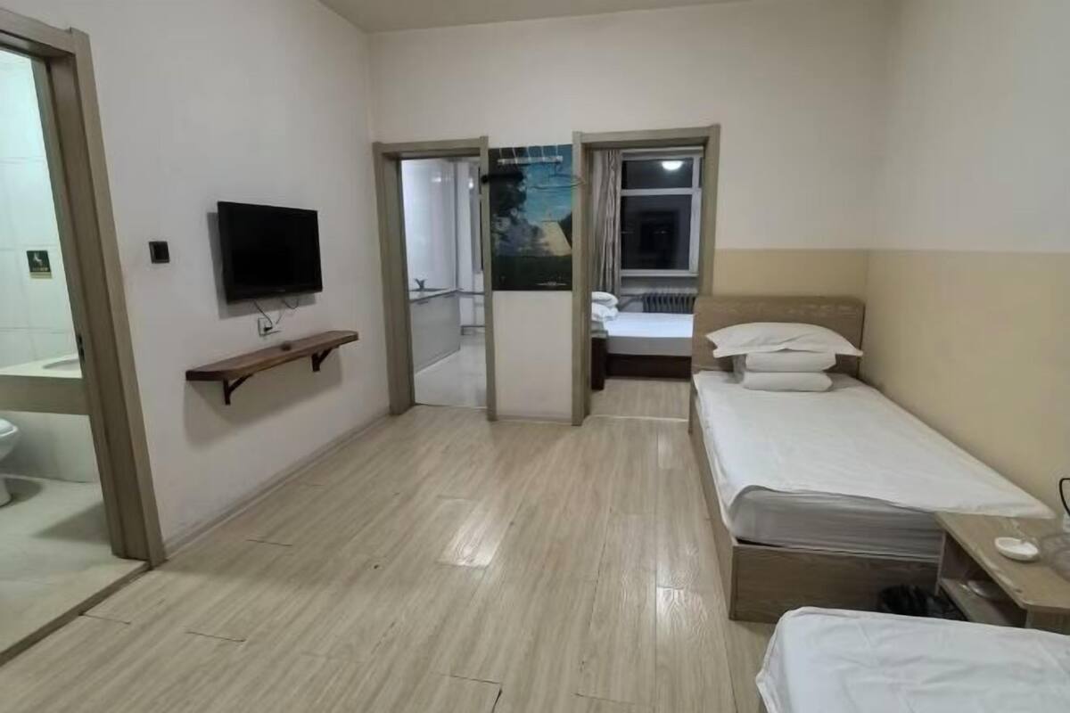 Hotellihuone, jossa on kaksi sänkyä, televisio, pieni hylly ja ikkuna, jossa on verhot.
