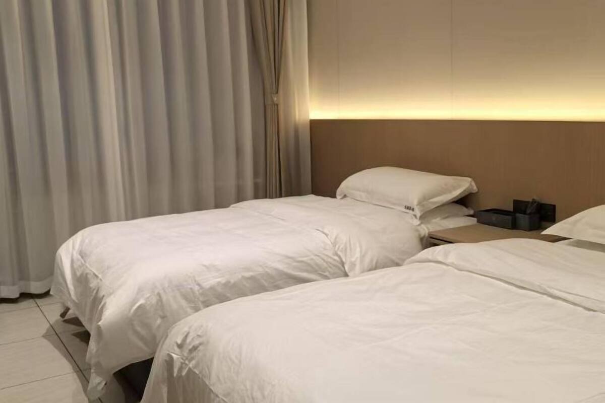 Hotellihuone, jossa on kaksi sänkyä, yöpöytä ja verho.