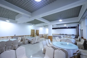 Un salón de conferencias con mesas y sillas redondas, paredes blancas y un techo con diseños tipo cuadrícula.