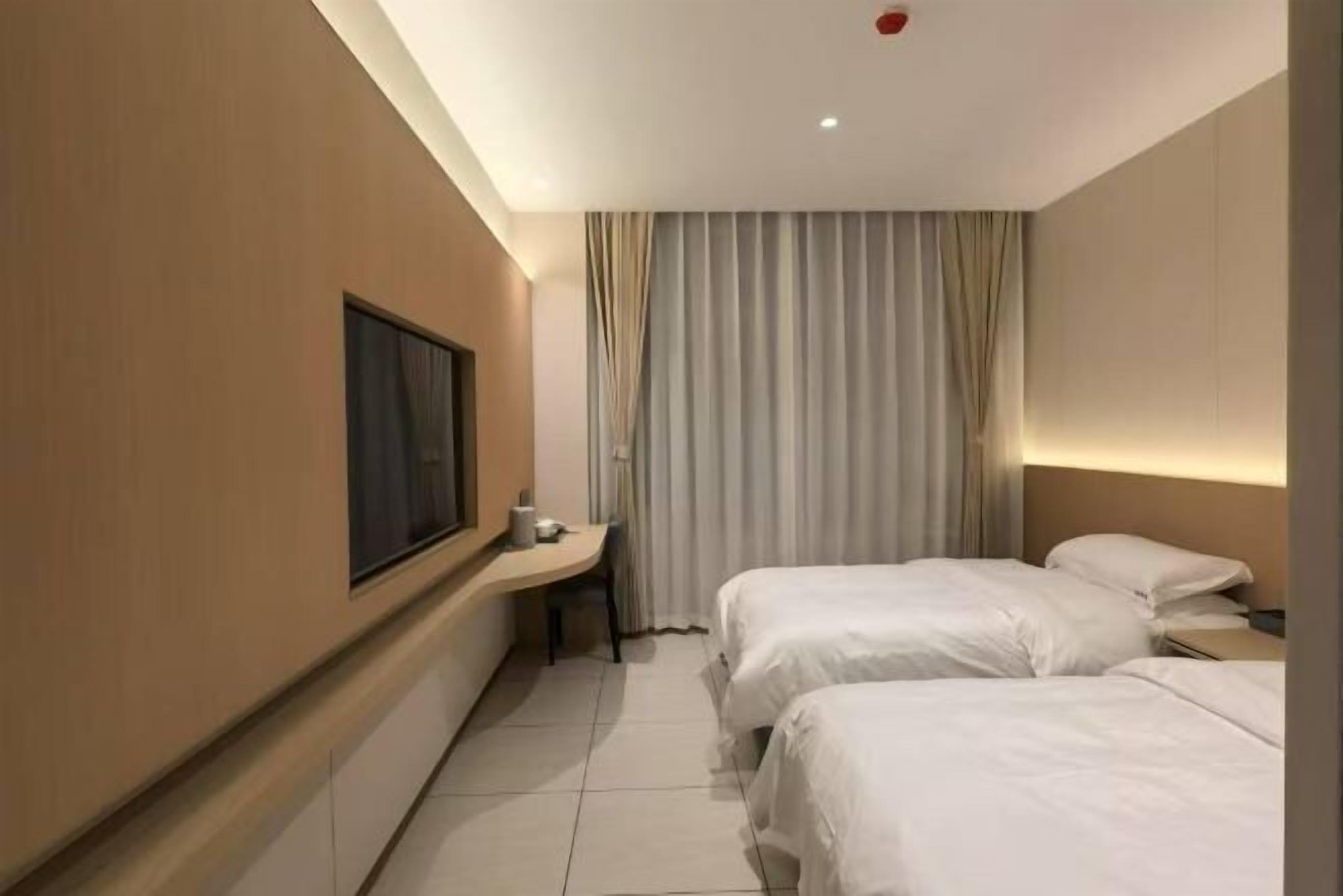 A hotel room with two beds, a desk, a chair, and a large window.