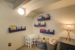 Una stanza piccola con un tavolo bianco, una sedia e una lampada. Si vedono scaffali con libri sulle pareti.