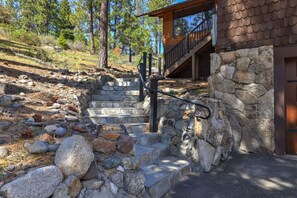 A stone staircase leading to a wooden cabin with a stone wall and a metal railing.