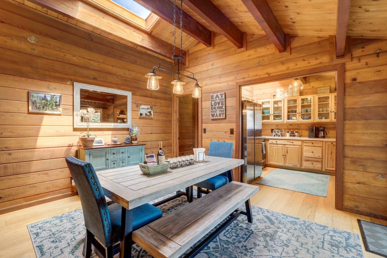 A wooden interior with a dining table, chairs, a bench, a kitchen area, and a skylight.