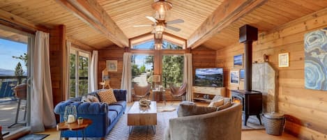 A spacious living room with a high ceiling, a fireplace, a television, and a view of the outdoors.