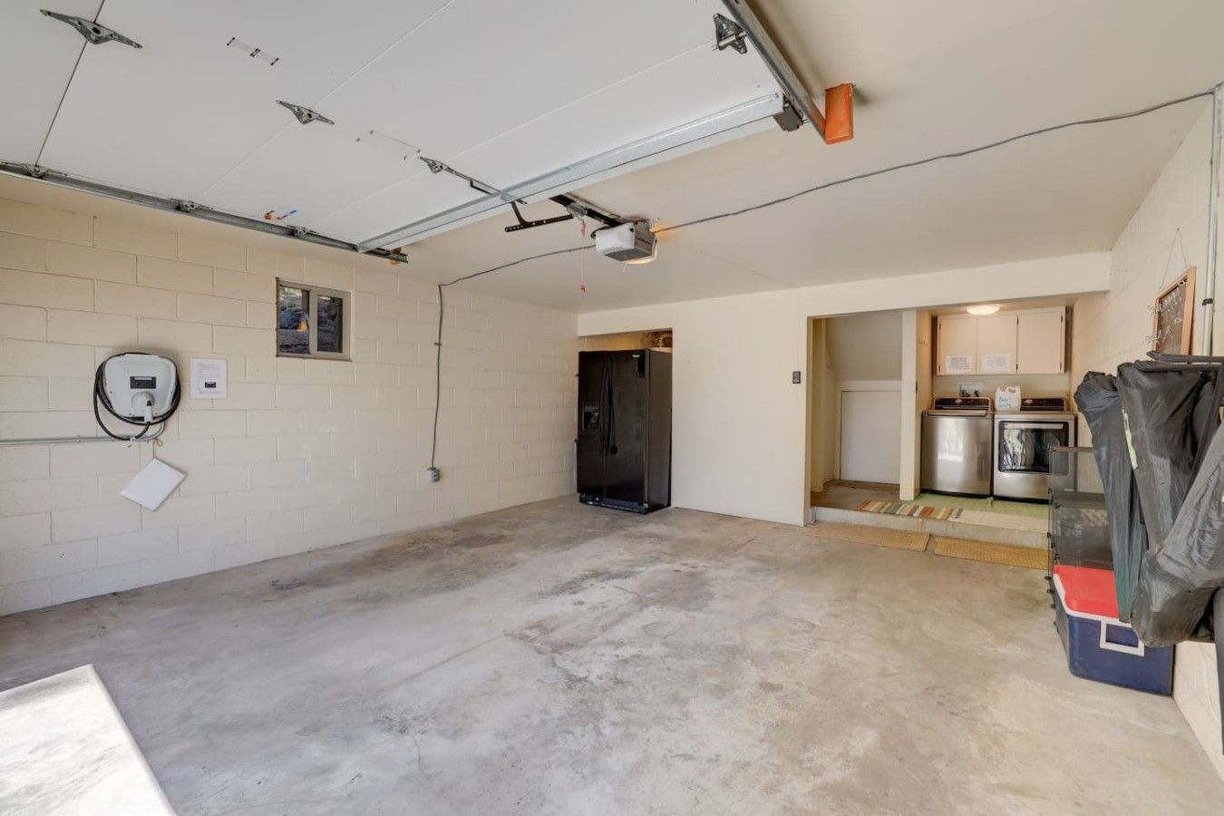 Eine Garage mit Betonboden, einem schwarzen Kühlschrank und einer Tür zu einem Küchenbereich mit Herd und Backofen.