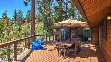 A wooden deck with outdoor furniture, a barbecue grill, and a glass door leading to a covered area.