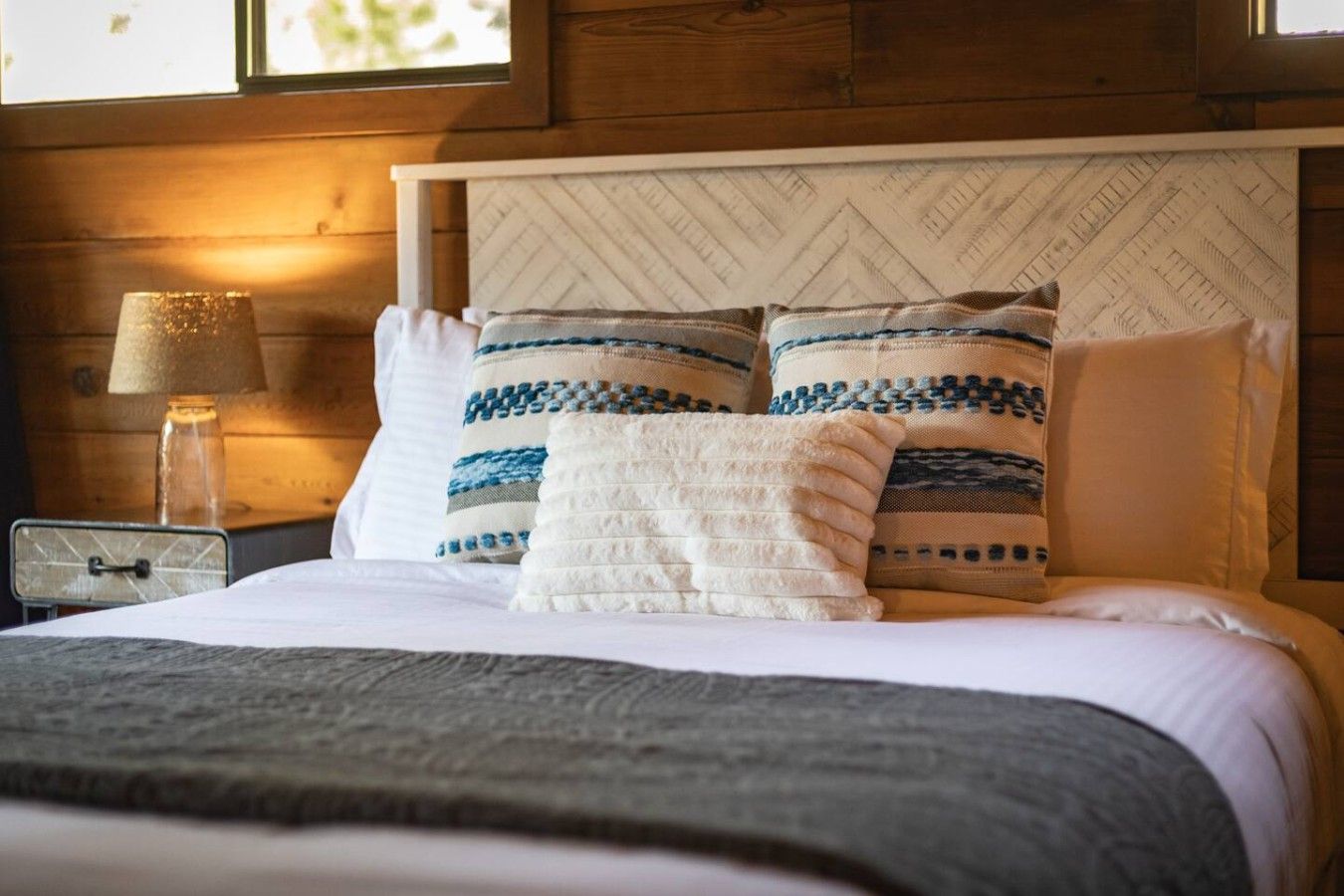 A bed with a white headboard, two pillows with blue and white patterns, and a gray blanket.