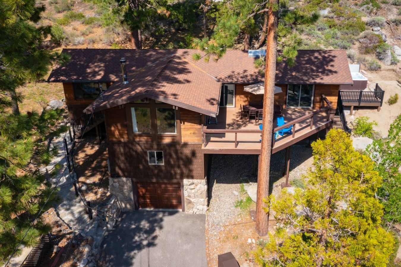 A two-story house with a deck, surrounded by trees and a rocky landscape.