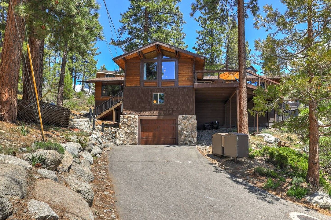 Eine zweistöckige Holzhütte mit Steinfundament, Garage und überdachter Veranda.