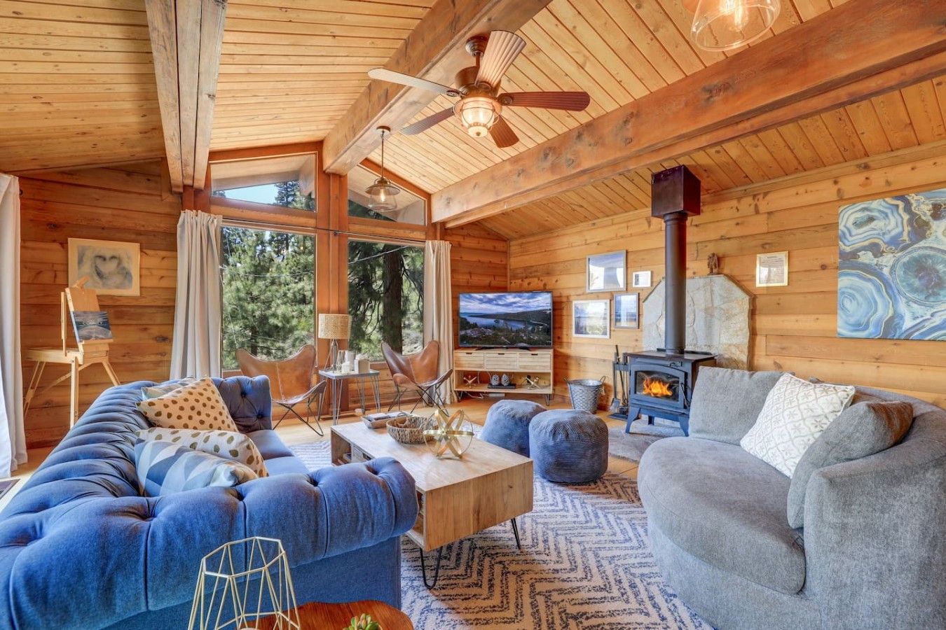 Ein gemütliches Blockhaus-Interieur mit einer Couch, Sesseln, einem Fernseher und einem Kamin.