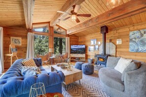 Un intérieur de chalet chaleureux avec un canapé, des fauteuils, un téléviseur et une cheminée.