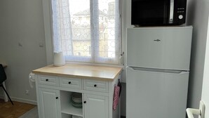 Eine kompakte Küche mit einem weißen Kühlschrank, einer Mikrowelle, einer Holz Arbeitsplatte und einem Fenster mit gemusterten Vorhängen.