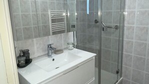 Ein modernes Badezimmer mit einem weißen Waschtisch, einer Glasdusche und Fliesenboden.