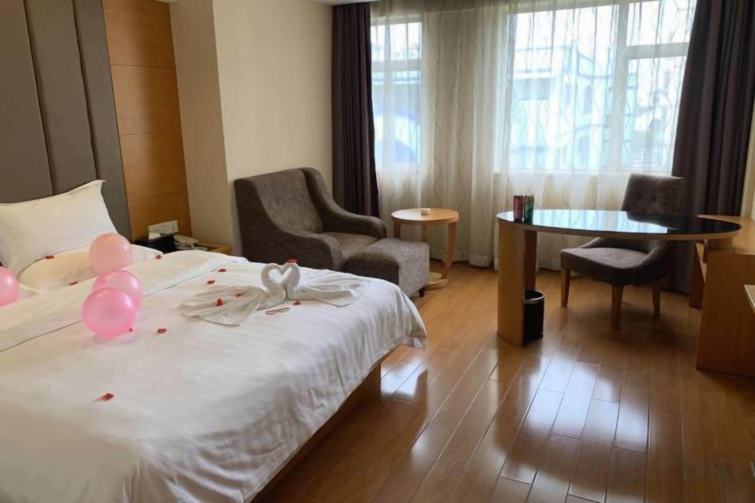 A hotel room with a bed, two armchairs, a small table, and a window with curtains.