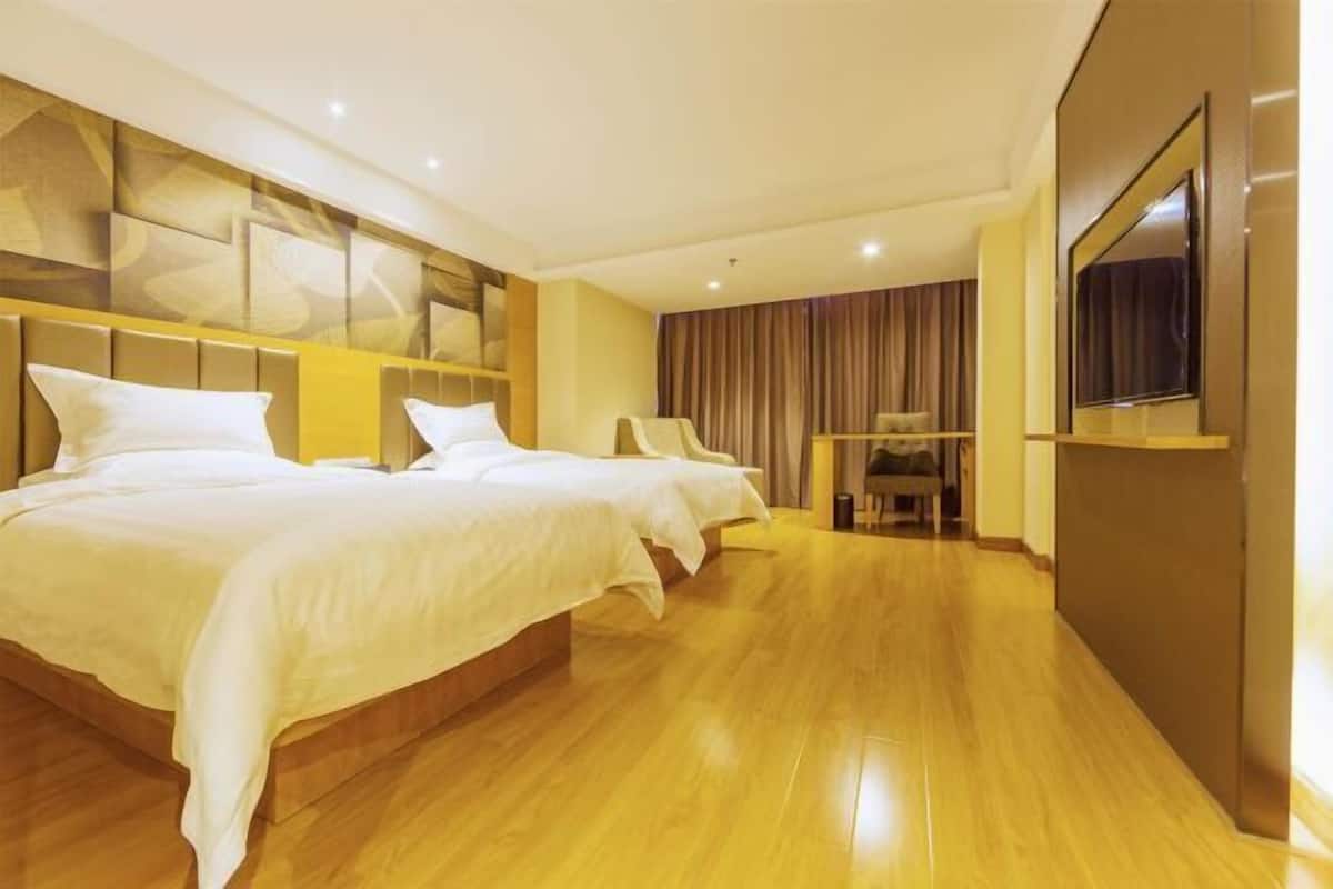 Una habitación de hotel con dos camas, un televisor de pantalla plana y piso de madera.