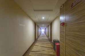 En lång, smal hotellkorridor med ett mönstrat golv, en papperskorg och en väggpanel av trä med en skylt.