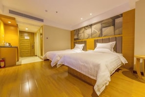 Habitación de hotel con dos camas, suelo de madera, cabecero moderno y una mesita de noche pequeña.