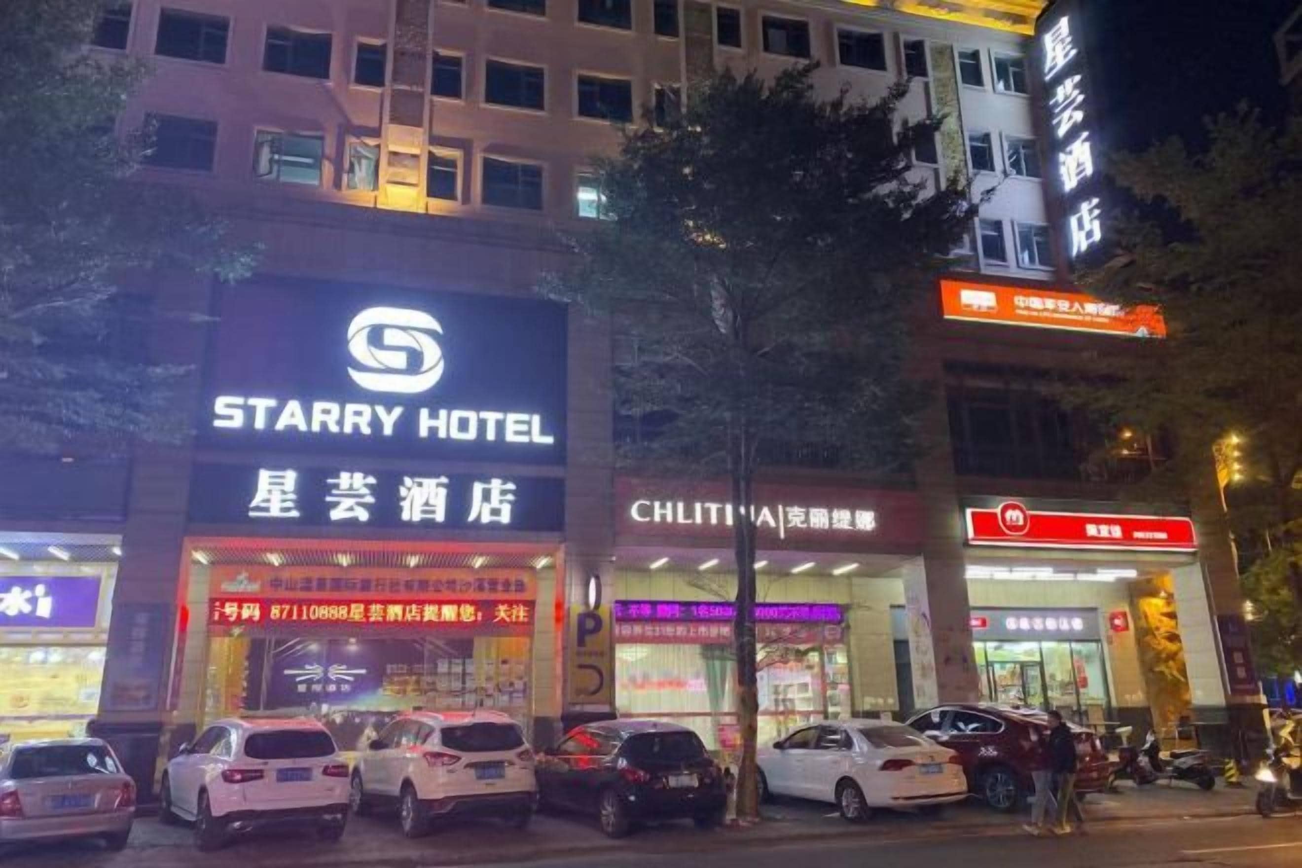 A hotel with a prominent sign, multiple parked cars, and a visible storefront with signage.
