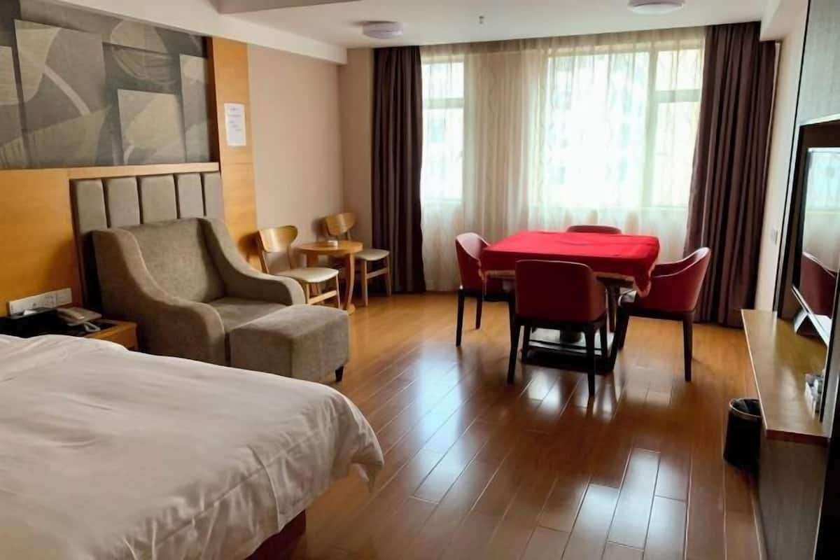 Habitación de hotel con cama, sofá, mesa de comedor con sillas, televisor y ventana con cortinas.