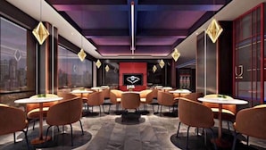 Een modern interieur met ronde tafels en oranje stoelen, een rode accentmuur en een stadszicht door grote ramen.