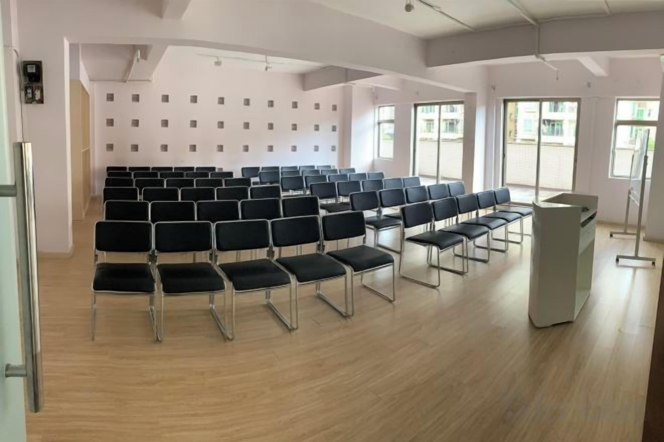Une salle de conférence avec des rangées de chaises, un pupitre et de grandes fenêtres.