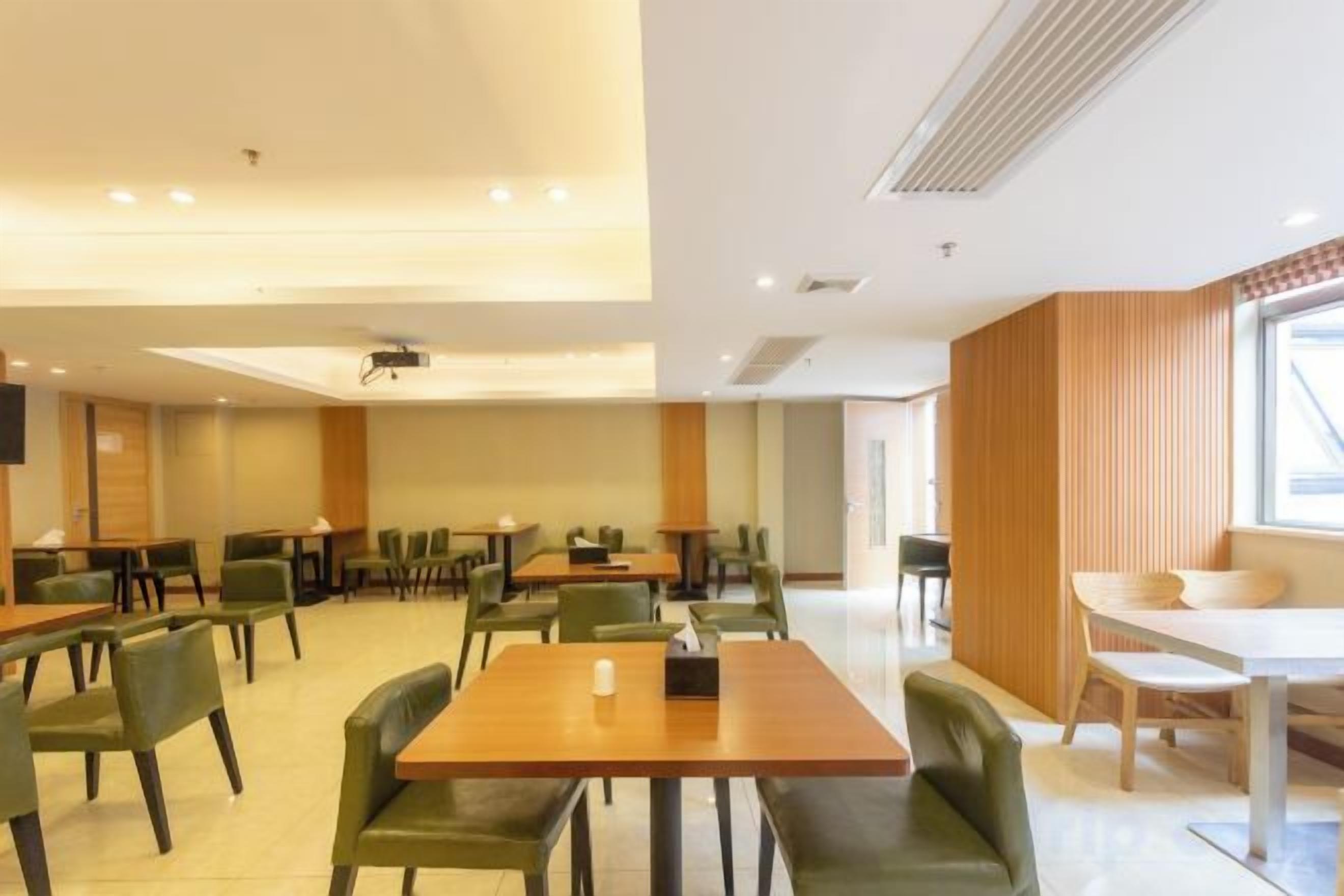 A spacious dining area with multiple tables and chairs, a projector screen, and a large window providing natural light.