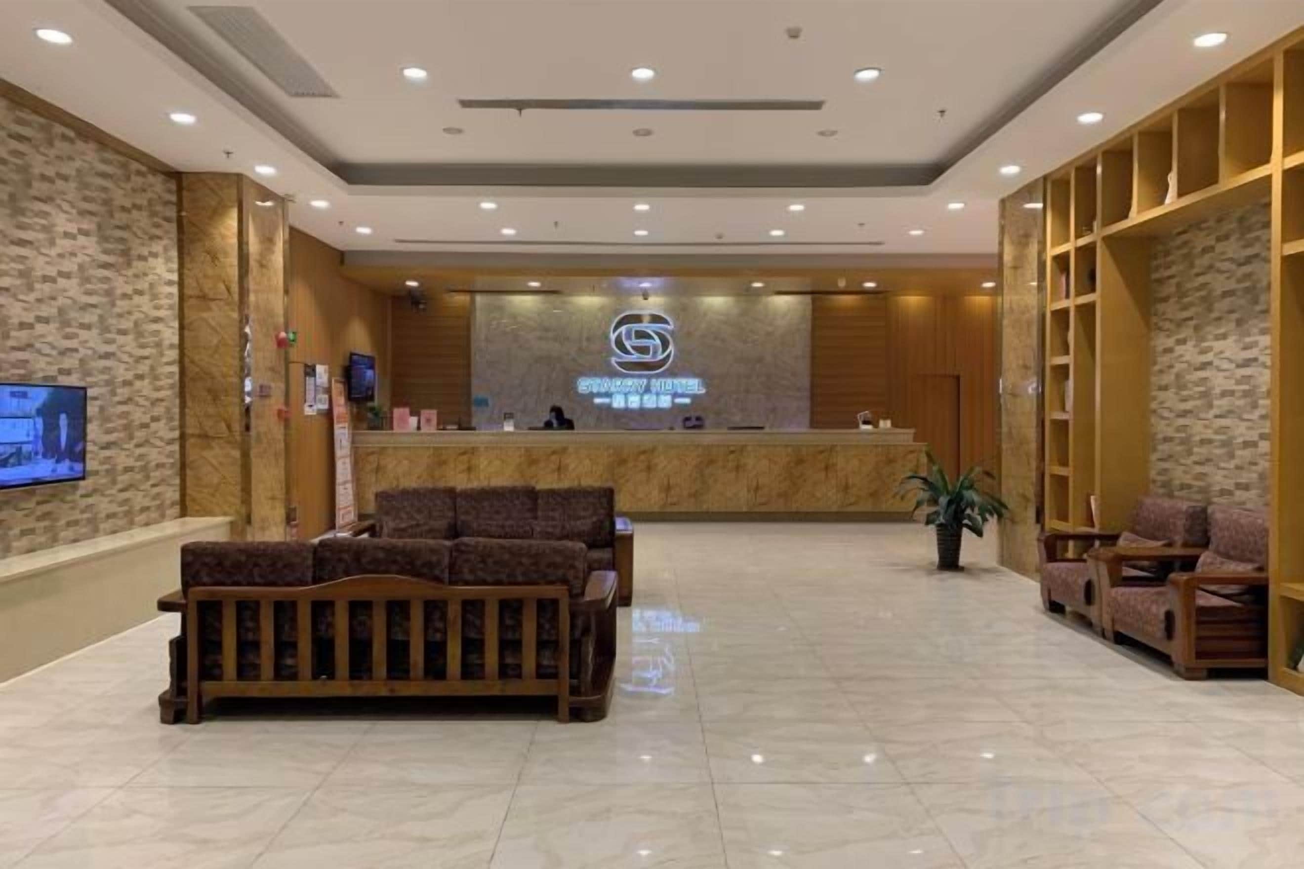 A hotel reception area with a reception desk, seating area, and a television screen.