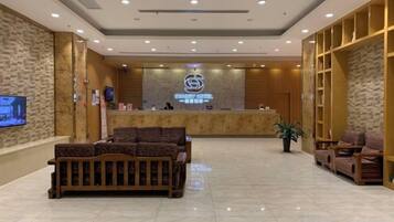 A hotel reception area with a reception desk, seating area, and a television screen.