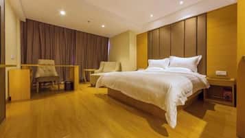 Ein modernes Hotelzimmer mit einem großen Bett, einer Sitzecke mit Sessel und kleinem Tisch, Holzböden und einem Vorhang im Hintergrund.