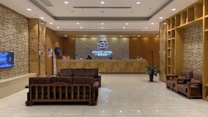 Een hotel lobby met een receptiebalie, een zithoek en een groot scherm.