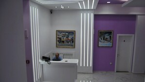 A reception area with a white desk, a man seated behind it, and two framed paintings on the walls. - White City  Hotel & Restaurant (Berat)