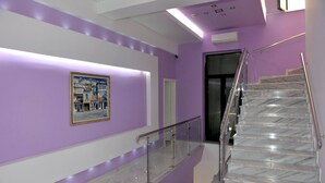 A modern interior with a purple wall, a framed cityscape painting, a glass railing, and a marble staircase.