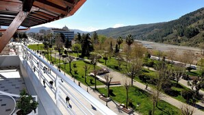 A balcony with a view of a park, a river, and distant mountains.