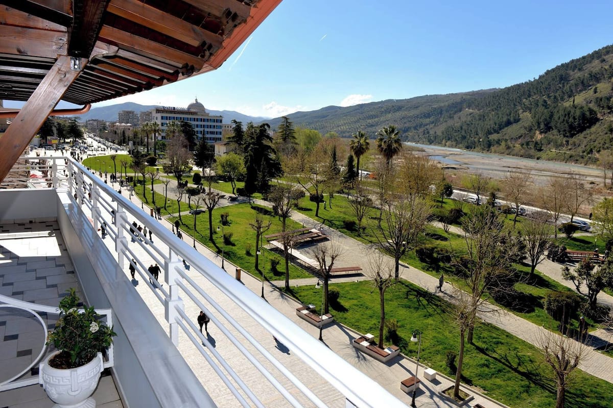 Un balcon avec vue sur un parc, une rivière et des montagnes lointaines.