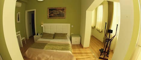A bedroom with a bed, nightstands, a painting, and a treadmill.