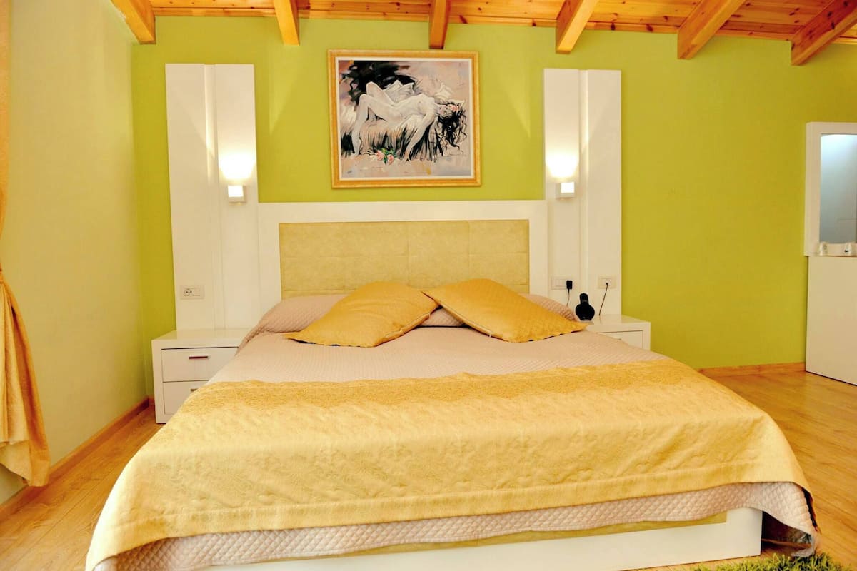 Une chambre à coucher avec un lit, une table de chevet, une lampe fixée au mur et un tableau accroché au mur.