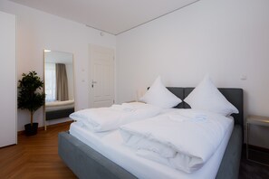 A hotel room with a bed, a potted plant, a mirror, and a door.